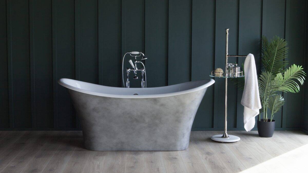 Elegant freestanding bathtub with chrome fixtures against dark green paneled wall, complemented by a modern metal towel stand, lush plant, and natural lighting—perfect for a luxurious bathroom setting.