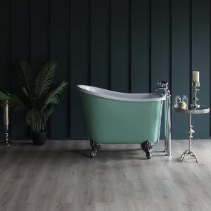 Elegant vintage-style freestanding bathtub in mint green with ornate clawfoot design, set against dark panelled walls with a contemporary wooden floor, complemented by luxurious bathroom accessories and lush greenery.