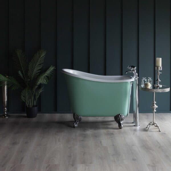 Elegant vintage-style freestanding bathtub in mint green with ornate clawfoot design, set against dark panelled walls with a contemporary wooden floor, complemented by luxurious bathroom accessories and lush greenery.