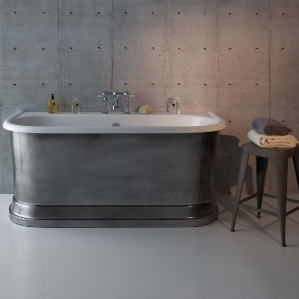 Polished freestanding bathtub with vintage-style chrome fittings, set against a concrete wall, with neatly folded towels on a rustic stool, showcasing modern luxury bathroom fixtures.