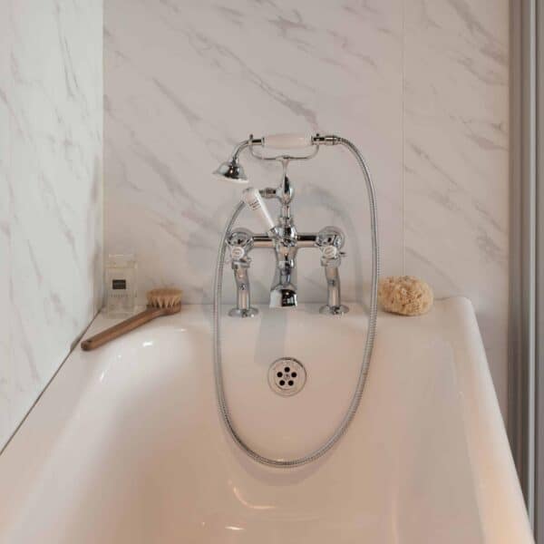 Elegant vintage-style bathtub with chrome fixtures and handheld shower, set against a luxurious marble wall, perfect for a classic bathroom design by The Albion Bath Co Ltd.