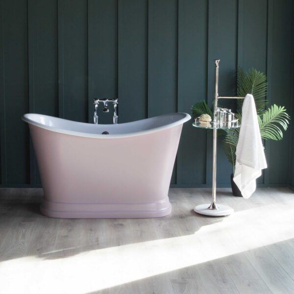 Elegant freestanding pink bathtub with vintage-style chrome fixtures against dark paneled wall, complemented by modern bath accessories and green plant for a luxurious bathroom setting.